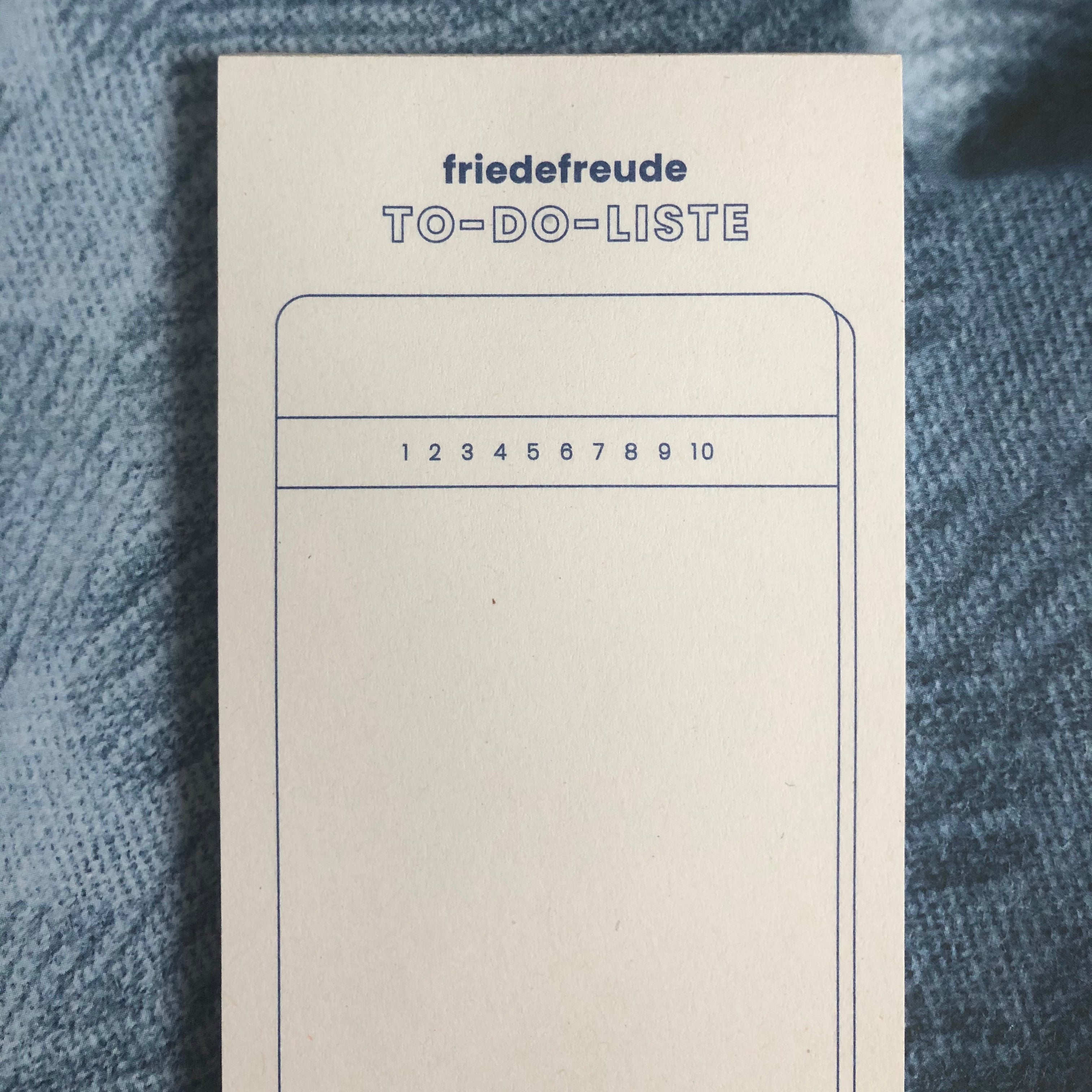 Notizblock mit der Aufschrift "friede freude TO-DO-LISTE" und nummerierten Zeilen von 1 bis 10 auf beigem Hintergrund.