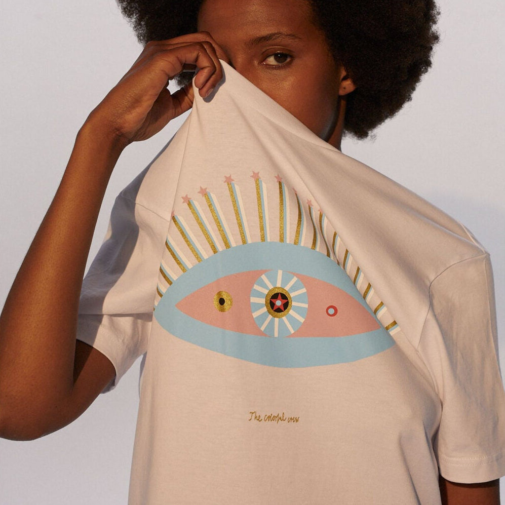 Person mit Afrofrisur hält ein T-Shirt mit farbigem Augendesign vor das Gesicht.